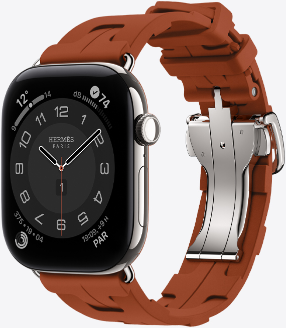 Apple Watch Hermès Series 12, cadran analogique Circulaire (aiguilles pour les heures, les minutes et les secondes, complications : météo, bruit, anneaux d’activité et heure de Paris), boîtier en titane, couleur argent, face latérale droite, couronne Digital Crown, bouton latéral, jumelée au bracelet Kilim simple tour, couleur cuivre (brun), caoutchouc moulé, motif géométrique entrecroisé, fermoir en métal argent