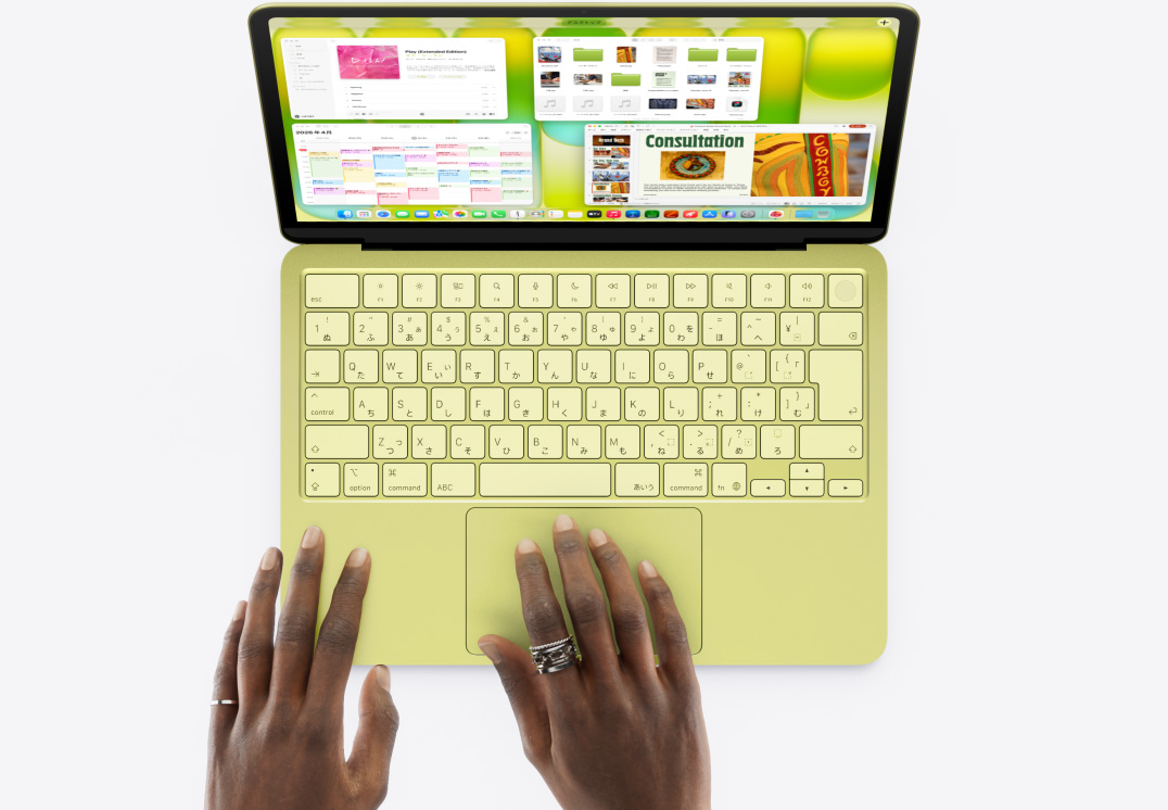 シトラスのMacBook Neo。トラックパッドに手が置かれている。ミュージック、カレンダー、Microsoft PowerPointアプリなど、複数のウインドウが開いている