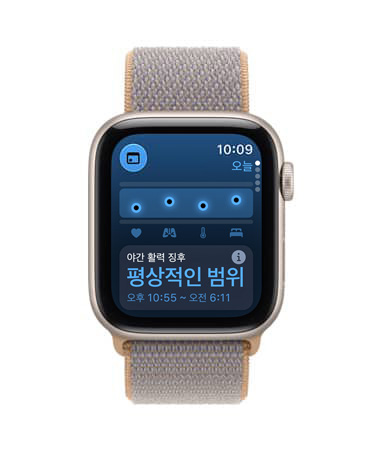 Apple Watch SE 3, 스타라이트 색상 알루미늄 케이스 및 건강 추적(활력 징후) 앱이 화면에 표시되고 오른쪽 옆면 외관에 Digital Crown 다이얼을 보여주는 모습. 샴브레이 블루(연한 블루 그레이 계열) 색상 스포츠 루프 밴드