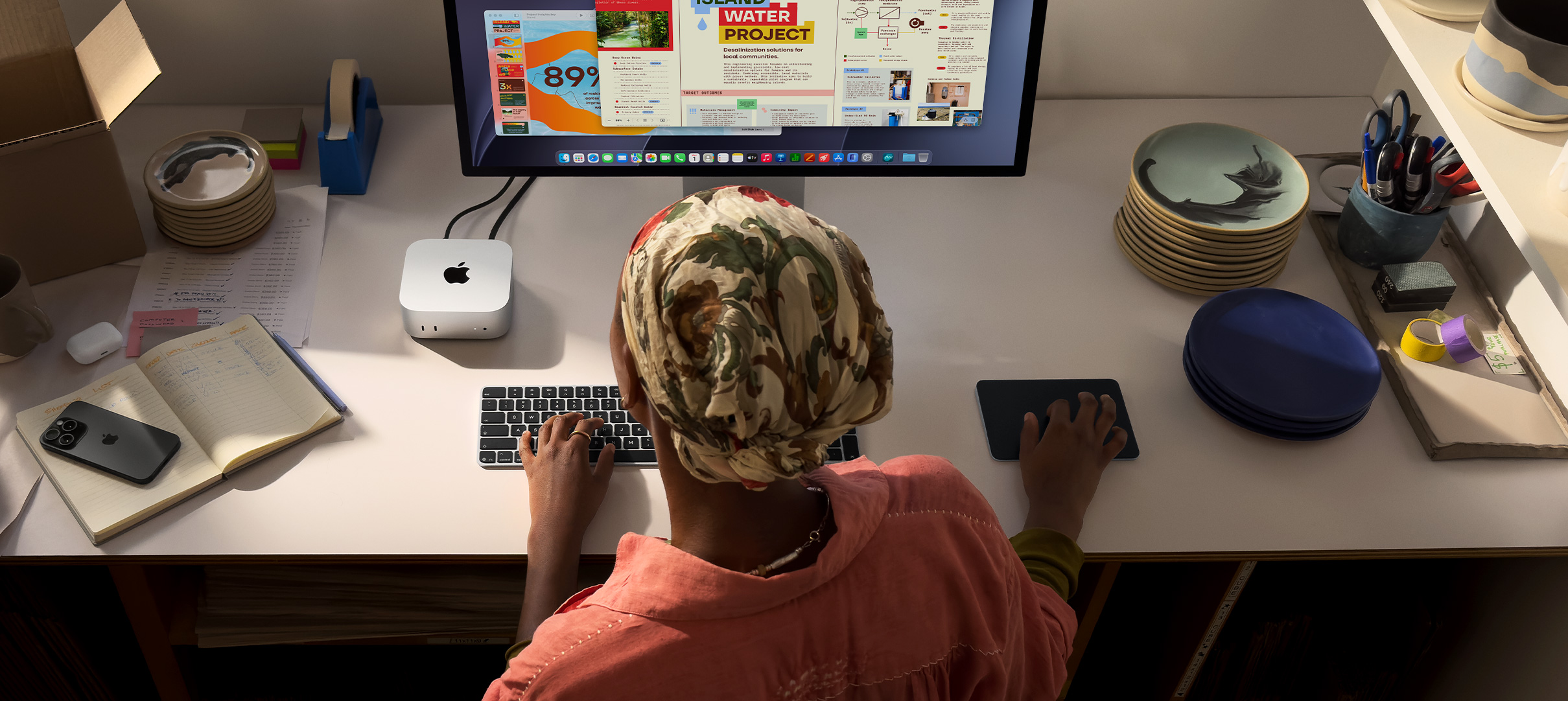 A person typing at a desk with a Mac&nbsp;mini, Studio&nbsp;Display connected, Magic&nbsp;Keyboard, Magic&nbsp;Trackpad, various items