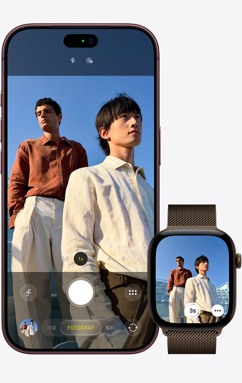 iPhone 18 Pro, önden dış görünüm, mavi gökyüzünün önünde duran iki adamın fotoğrafını çekmek için kamera kullanılıyor, yanında duran Apple Watch Ultra 3’ün ekranında Kamera Kumandası uygulaması açık