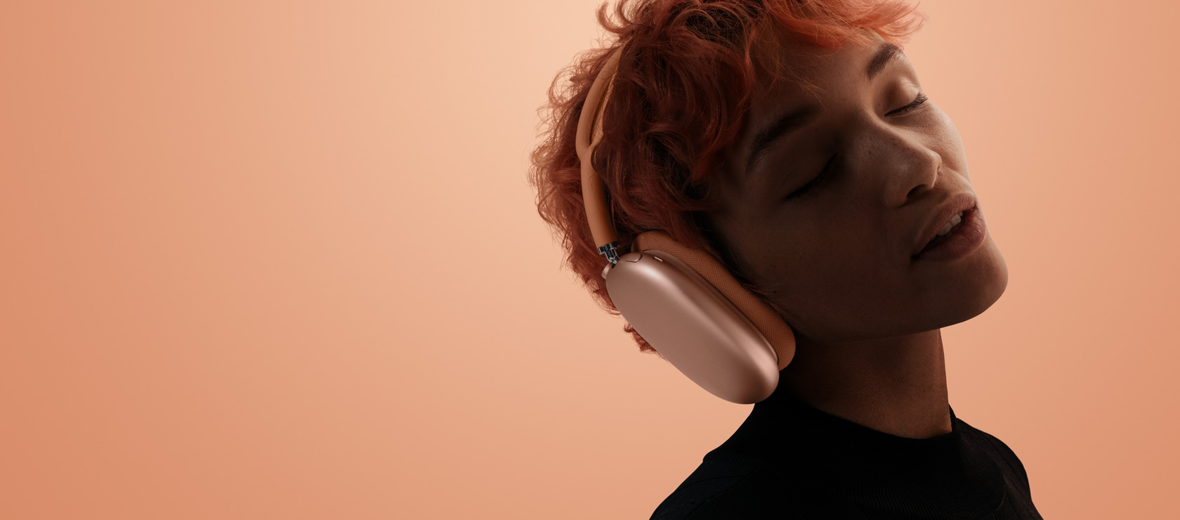 شخص رأسه مائل وعيناه مغلقتان يضع AirPods Max 2 على رأسه، لون برتقالي، على خلفية بلون برتقالي وردي