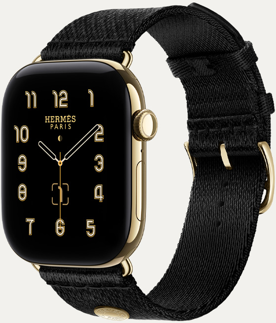Apple Watch Hermès Series 12, Clou de Selle 아날로그 시계 페이스, 시, 분, 초침, 컴플리케이션에 월령 달력, 날짜가 표시된 모습. 래디언트 골드 색상의 티타늄 케이스의 오른쪽 옆면 외관에 Digital Crown과 측면 버튼을 보여주는 모습. 시계 케이스와 어울리는 래디언트 골드 하드웨어가 달린 매끄러운 블랙 새틴 웨빙 소재의 누아 새틴 Clou de Selle 밴드와 페어링되어 있는 모습