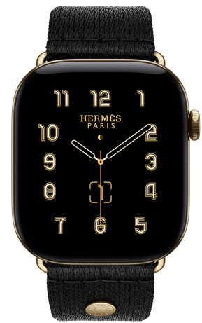 Apple Watch Hermès Series 12, Clou de Selle 아날로그 시계 페이스, 시, 분, 초침, 컴플리케이션에 월령 달력, 날짜가 표시된 모습. 래디언트 골드 색상의 티타늄 케이스의 오른쪽 옆면 외관에 Digital Crown과 측면 버튼을 보여주는 모습. 시계 케이스와 어울리는 래디언트 골드 하드웨어가 달린 매끄러운 블랙 새틴 웨빙 소재의 누아 새틴 Clou de Selle 밴드와 페어링되어 있는 모습