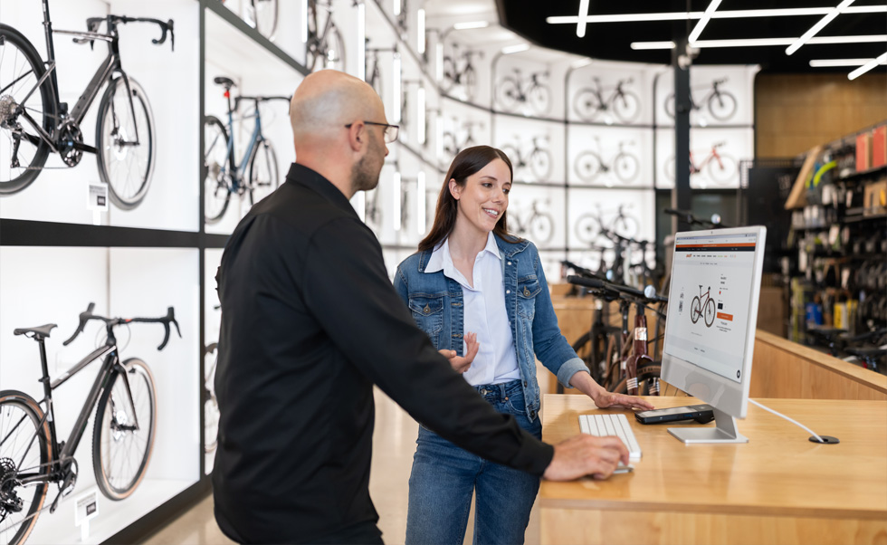 Julien Sicuro, Store Manager, begleitet eine Kundin mithilfe des kristallklaren Retina Displays des iMac durch die Fahrradauswahl.