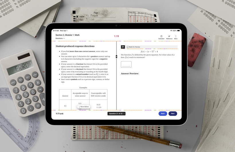 Un iPad sobre un escritorio junto a formularios de evaluación tradicionales y útiles escolares. En la pantalla, se muestran instrucciones para completar la sección de matemáticas de un examen estandarizado.