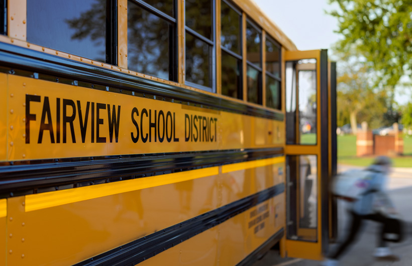 Primer plano de la parte lateral de un autobús escolar del Fairview School District, mientras un estudiante baja del autobús.