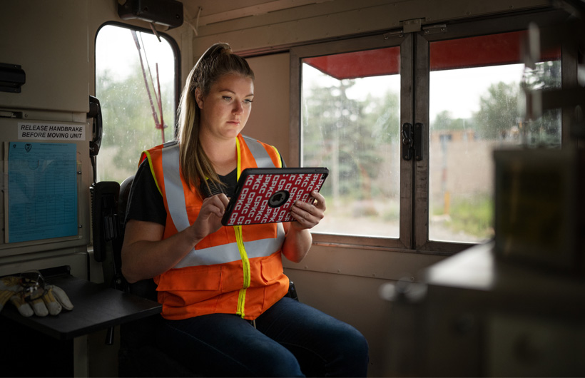 Una trabajadora ferroviaria sentada dentro de un vagón de tren parado consulta un iPad