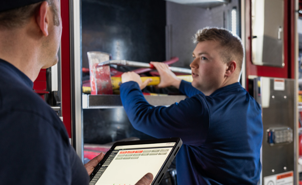 To brandfolk gennemgår værktøjet og udstyret på en brandbil – den ene med en iPad i hånden, mens den anden inspicerer 