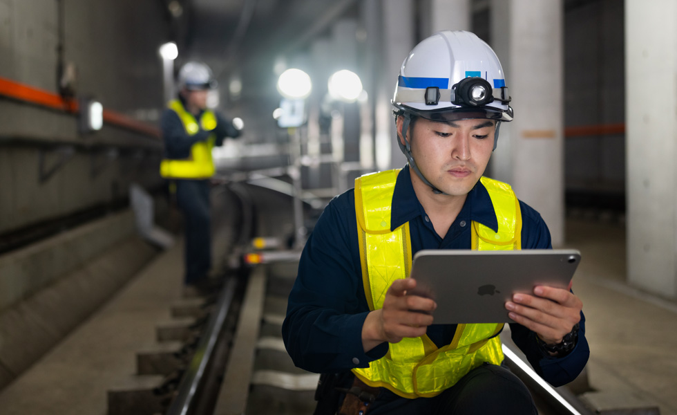 En arbeider med sikkerhetsvest og hjelm ser på en iPad mens det utføres vedlikehold i tunnelene til Tokyo Metro.