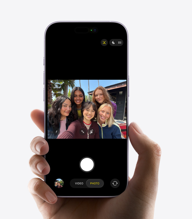 iPhone skats no priekšas, ar Center Stage priekšējo kameru tiek filmēts trīs cilvēku selfija video, ap sejām ir dzelteni kvadrāti, kas parāda automātisko kadrēšanu