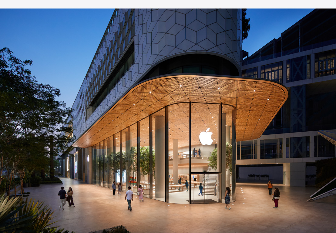 Apple veikals naktī, no iekšpuses izgaismoti stikla logi, virs ieejas durvīm centrā ir Apple logotips.