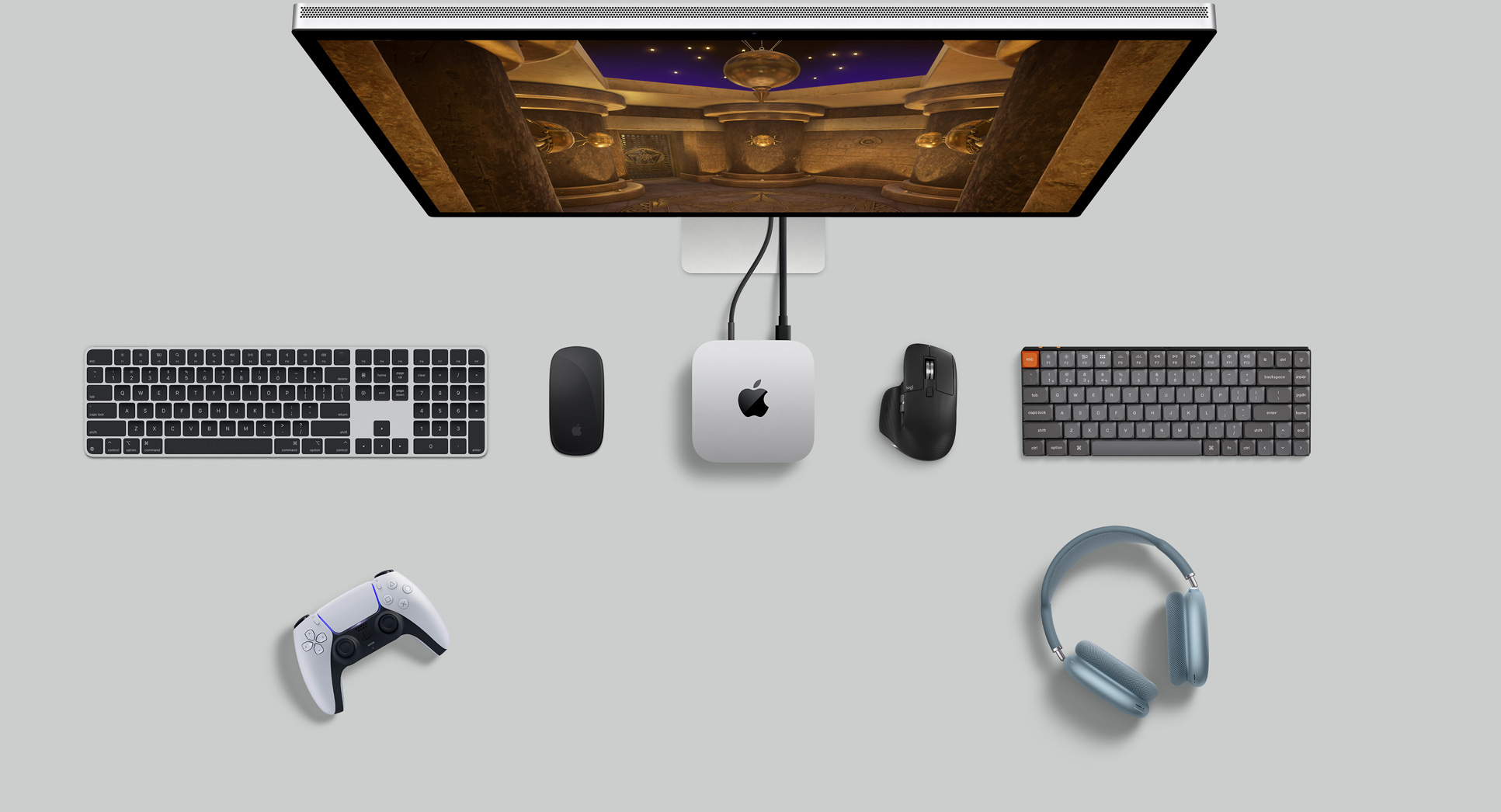 Вид зверху на сріблястий Mac mini, який розміщено на столі поряд із монітором з активним екраном, бездротовими клавіатурами, бездротовими мишами, ігровим контролером і навушниками AirPods Max