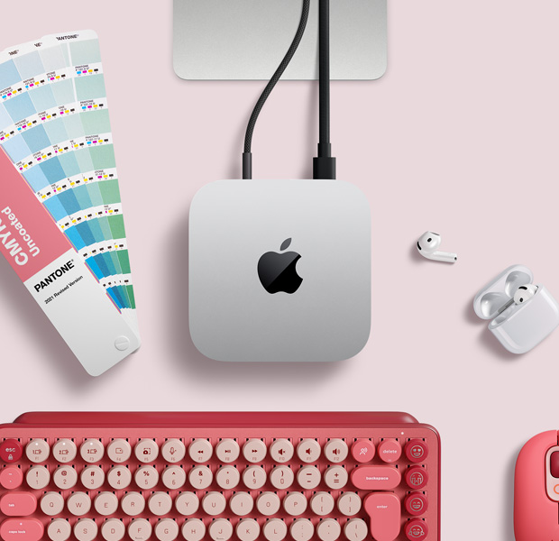 Вид зверху на сріблястий Mac mini. Поруч із ним на столі лежать навушники AirPods, рожева бездротова клавіатура, рожева бездротова миша та розсувна палітра кольорів