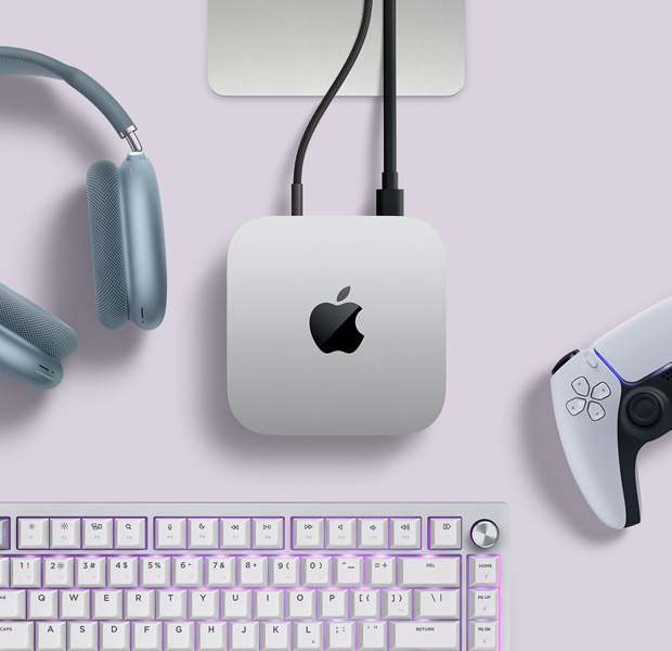 Вид зверху на сріблястий Mac mini з двома кабелями, під’єднаними до портів на задній панелі комп’ютера. Поруч із ним лежать навушники AirPods Max блакитного кольору, срібляста клавіатура Magic Keyboard і бездротовий ігровий контролер