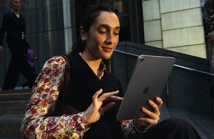 Seseorang yang duduk di tangga di luar bangunan besar sedang menggunakan iPad Air 11 inci berwarna Abu-abu, dengan koneksi Wi-Fi yang lancar di seluruh transfer jaringan